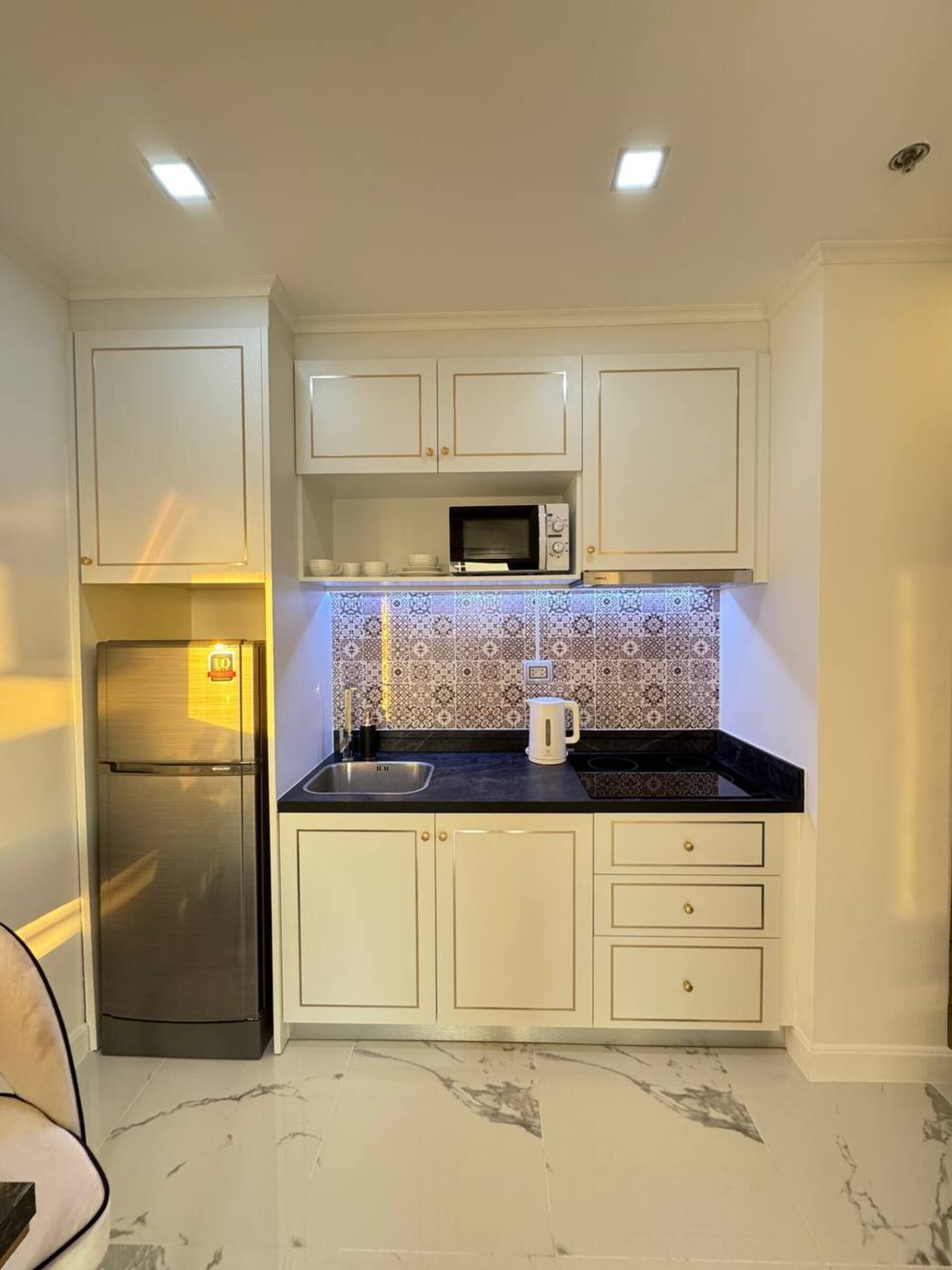 Una cocina compacta con gabinetes blancos, un refrigerador de acero inoxidable, un microondas y un salpicadero de azulejos.