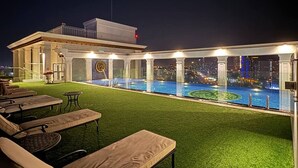 An outdoor pool area with lounge chairs and a view of the city skyline at night. - GSR-Empire Tower (Pattaya)