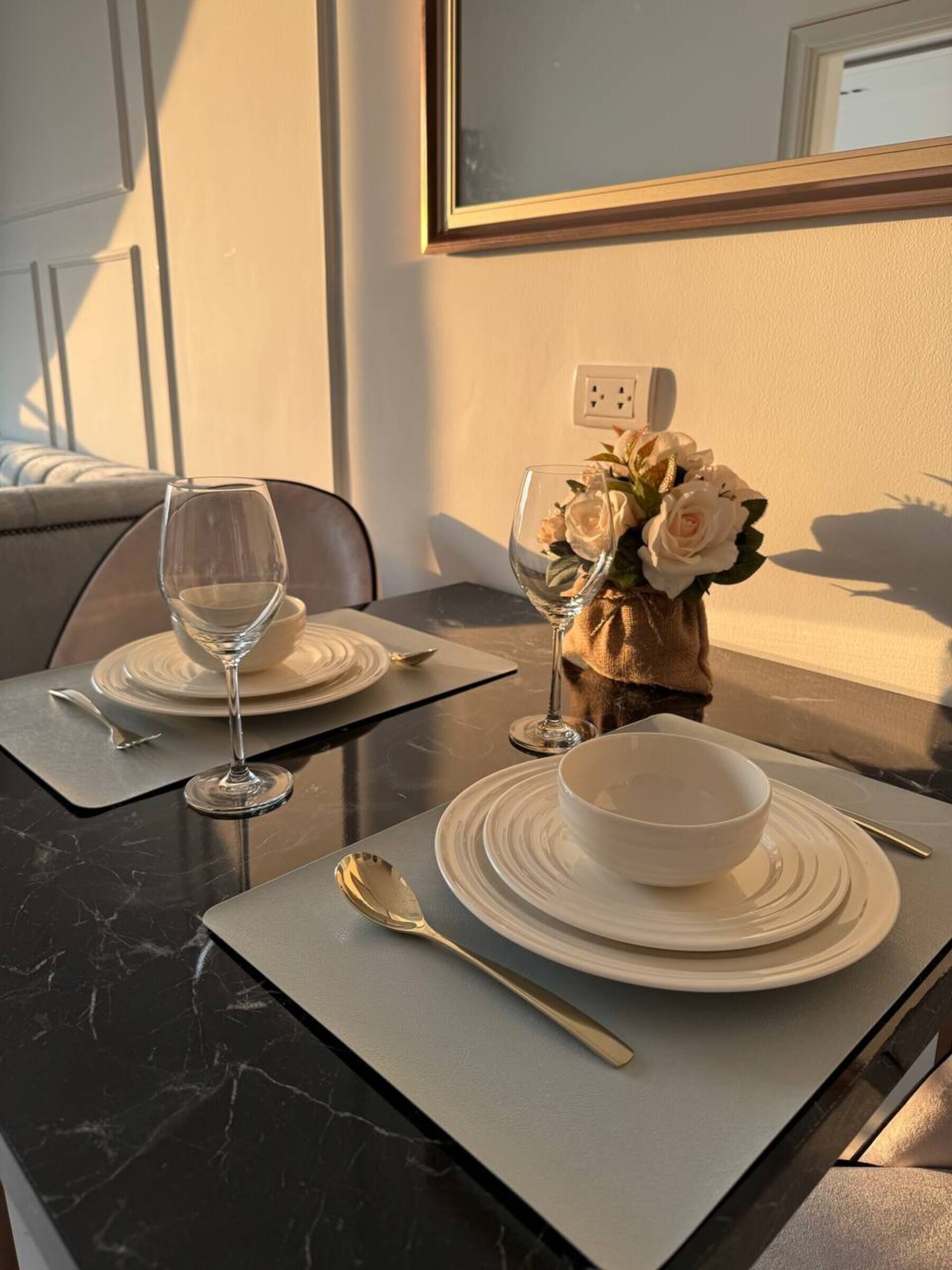 Uma mesa de jantar com um vaso de flores brancas, duas taças de vinho e uma tigela sobre uma mesa de mármore.