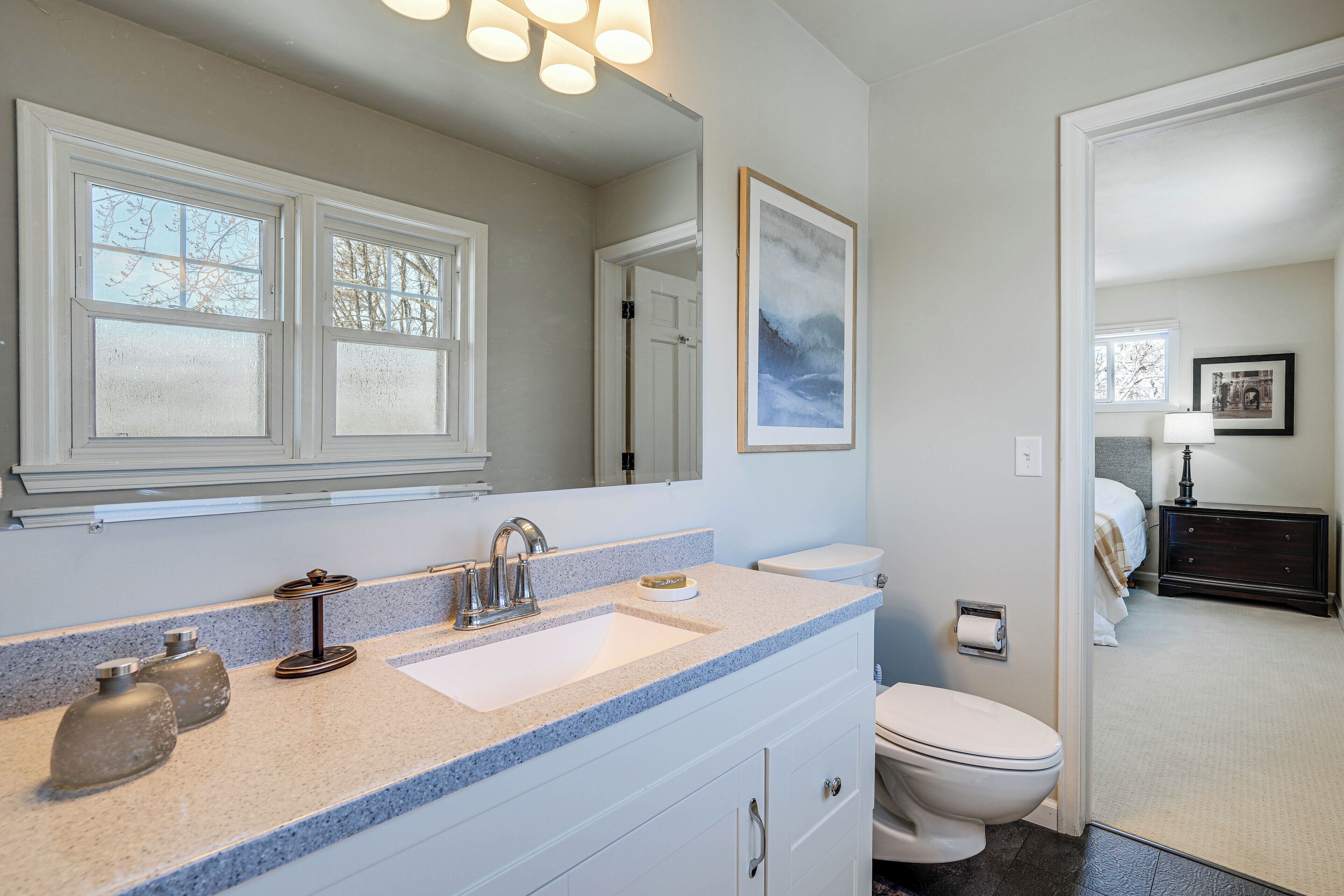 A bathroom with a white vanity, a large mirror, and a window above the sink.