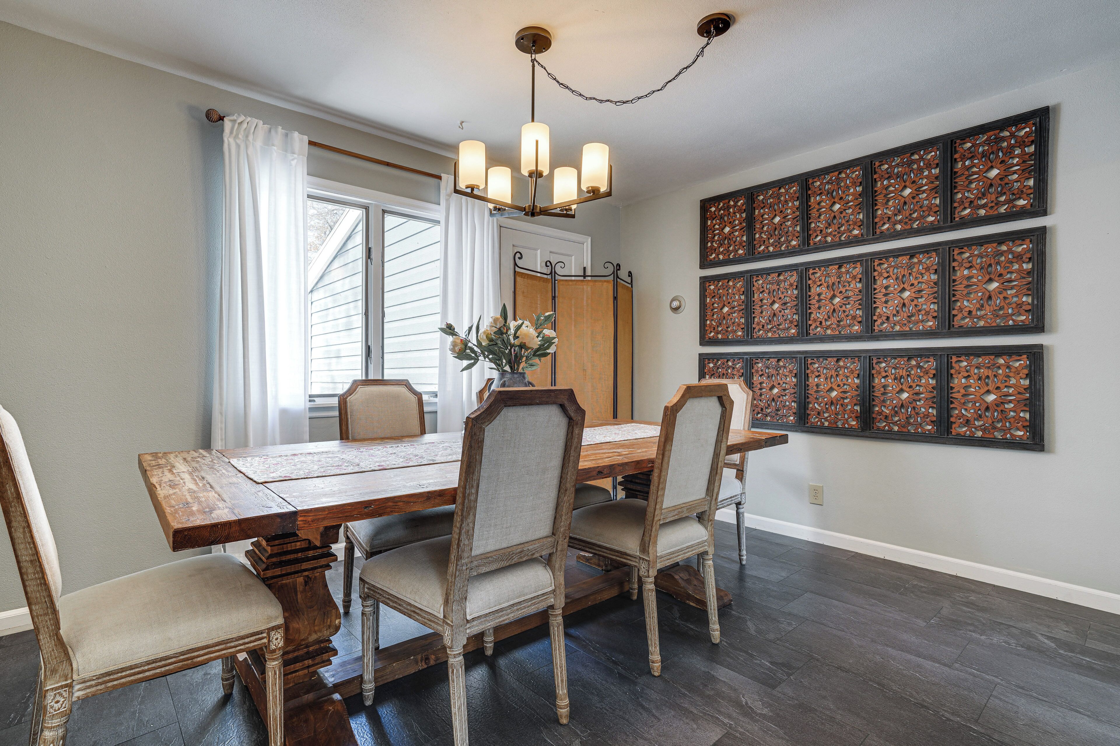 Comedor con una mesa y sillas de madera, una araña y decoración en las paredes.