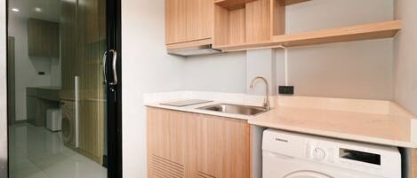 Una cocina compacta con lavadora integrada, un lavamanos y armarios de madera.