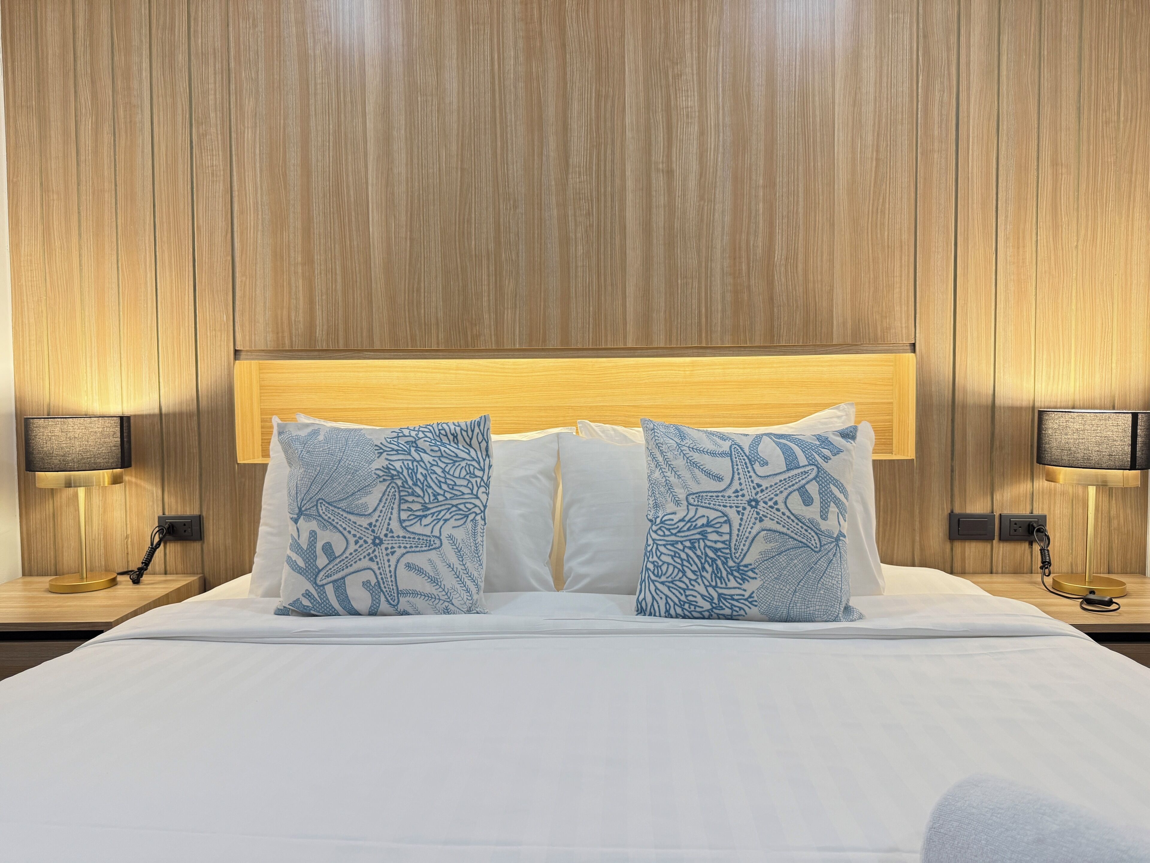 Un lit bien fait, avec du linge de lit blanc et deux coussins décoratifs ornés d’un motif bleu sur le thème de la mer.
