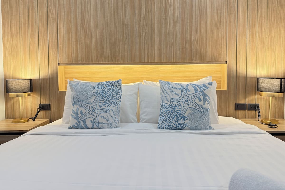 A neatly made bed with white linens and two decorative pillows featuring a blue sea-themed design.