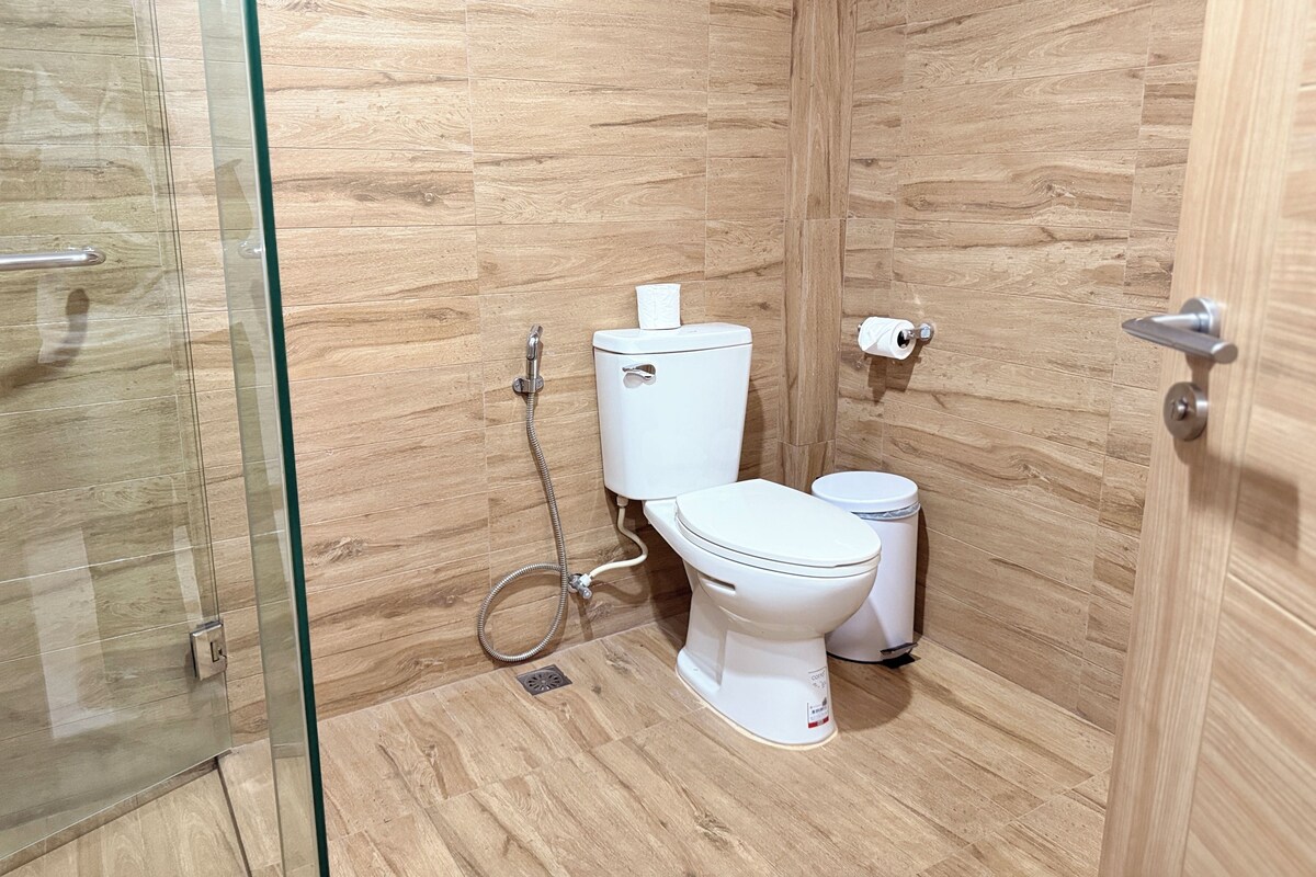 A bathroom with a glass shower enclosure, a toilet, and a trash bin.