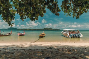 Une plage avec des bateaux, une eau cristalline et des montagnes à l’horizon.