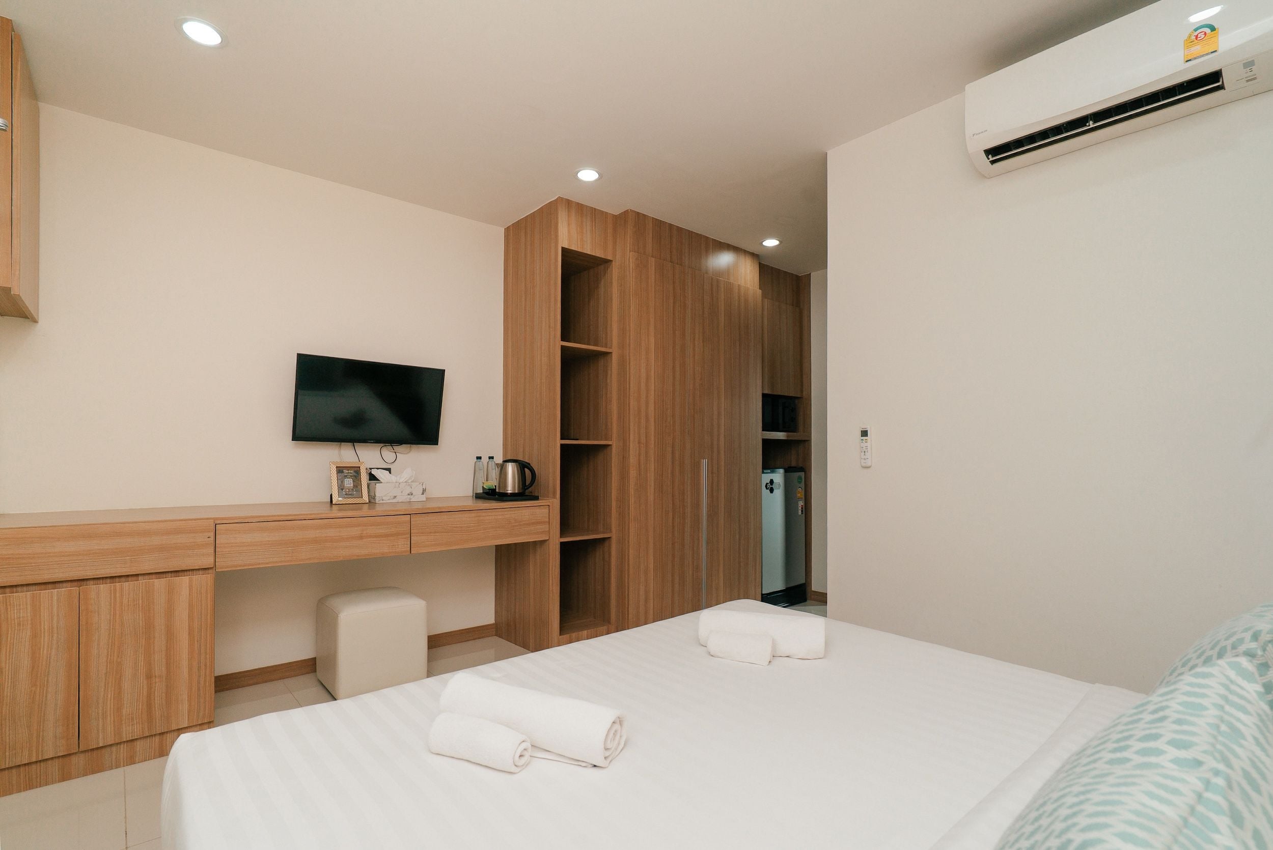 A hotel room with a bed, a desk with a flat-screen TV, a minibar, and a wardrobe.