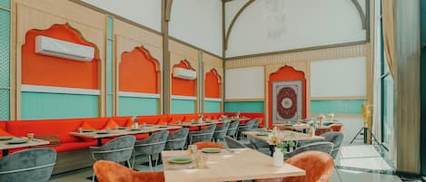 A restaurant with high ceilings, orange seating, and a patterned wall.