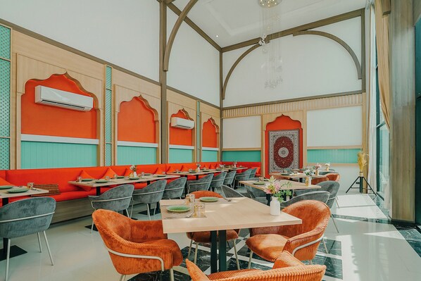Un restaurant avec de hauts plafonds, des sièges orange et un mur orné de motifs.