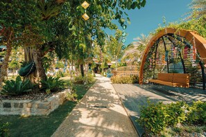 A pathway lined with trees and a wooden bench, leading to an arched structure with hanging decorations. - Love Rawai Hotel (Rawai)