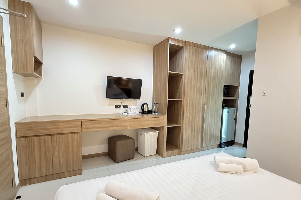 Ein modernes Hotelzimmer mit Schreibtisch aus Holz, einem Flachbildfernseher, einem großen Kleiderschrank und einem Bett mit ordentlich gefalteten Handtüchern.