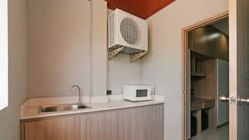 A compact kitchen with a built-in sink, a microwave, and a wall-mounted air conditioner.
