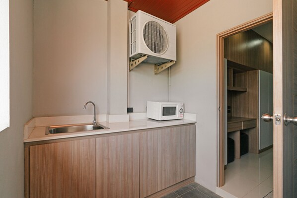 A compact kitchen with a built-in sink, a microwave, and a wall-mounted air conditioner. - Love Rawai Hotel (Rawai)