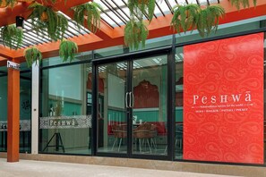 Un restaurante con fachada de vidrio, pared con diseño rojo y plantas colgantes.