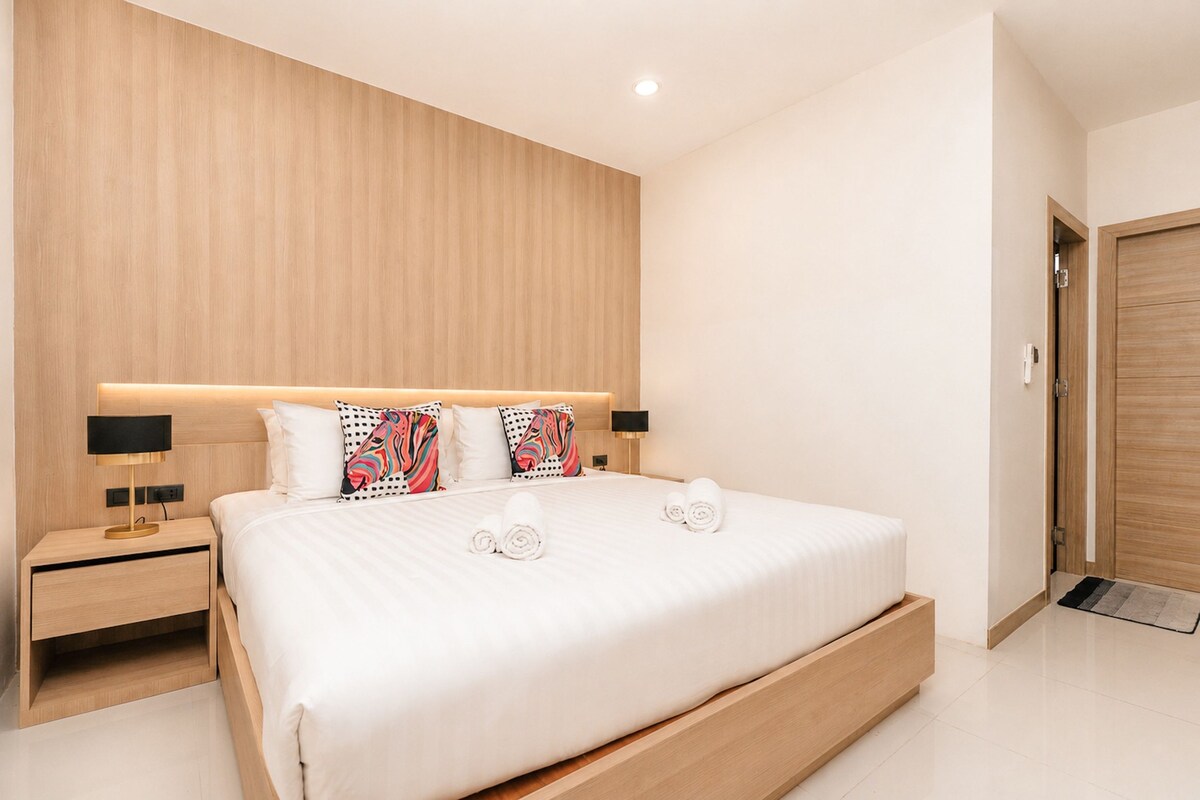 A modern bedroom with a large bed, bedside lamps, and a wooden headboard.