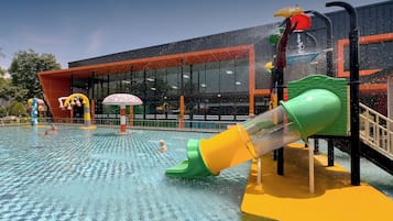 Zona de juegos acuáticos con toboganes y piscina, rodeada por un edificio de grandes ventanales y diseño moderno.