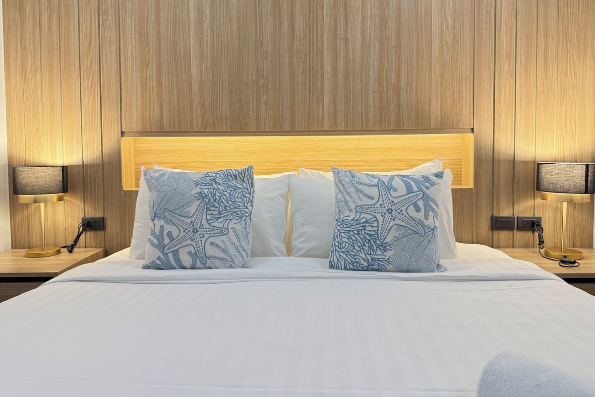 A hotel room with a wooden headboard, white bedding, and two decorative pillows with a blue pattern.