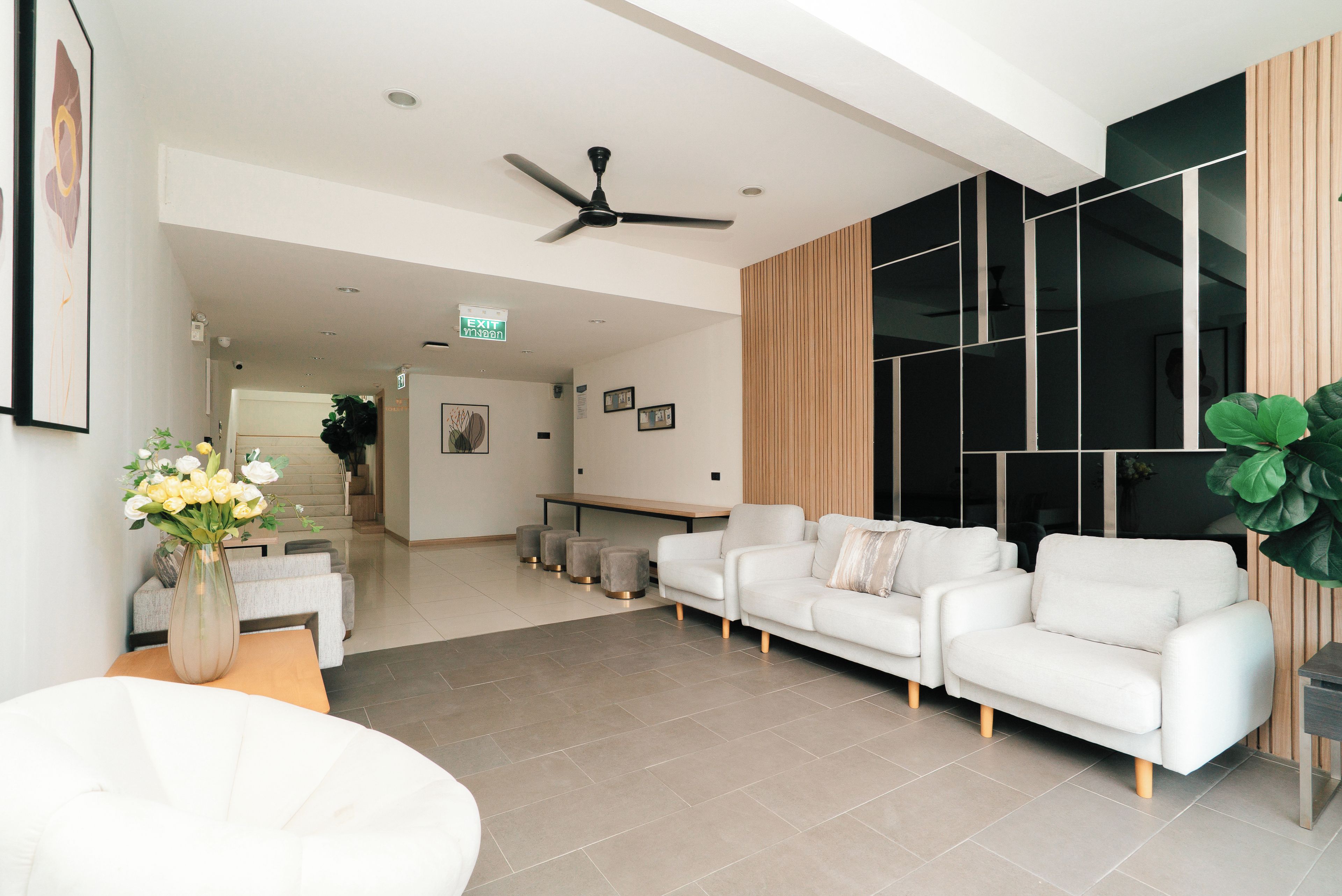 A modern living area with a white sofa set, a ceiling fan, and a large window with blinds.