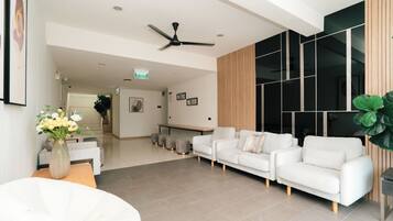 A modern living area with a white sofa set, a ceiling fan, and a large window with blinds.