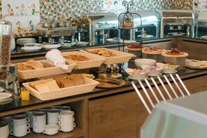 Un buffet con diversi cibi, tra cui pane, dolci e salumi, e un angolo caffè con tazze.