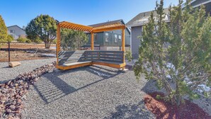 A wooden pergola with a bench in a gravel area, surrounded by trees and houses. - Show Low Home w/ Deck: Near Lake & Trails! (Show Low)