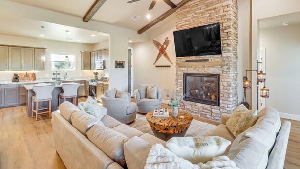 A spacious living area with a stone fireplace, comfortable seating, and a modern kitchen in the background. - Show Low Home w/ Deck: Near Lake & Trails! (Show Low)