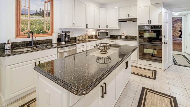 A modern kitchen with white cabinets, granite countertops, a large island, a built-in oven, and a window with a scenic view. - Pool Table + Private Porch: Peaceful Apt in Belle (Belle)