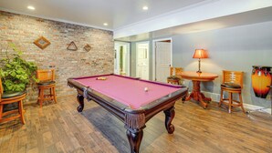 A pool table with chairs, a lamp, and a drum set in a room with wooden flooring and a brick wall. - Pool Table + Private Porch: Peaceful Apt in Belle (Belle)