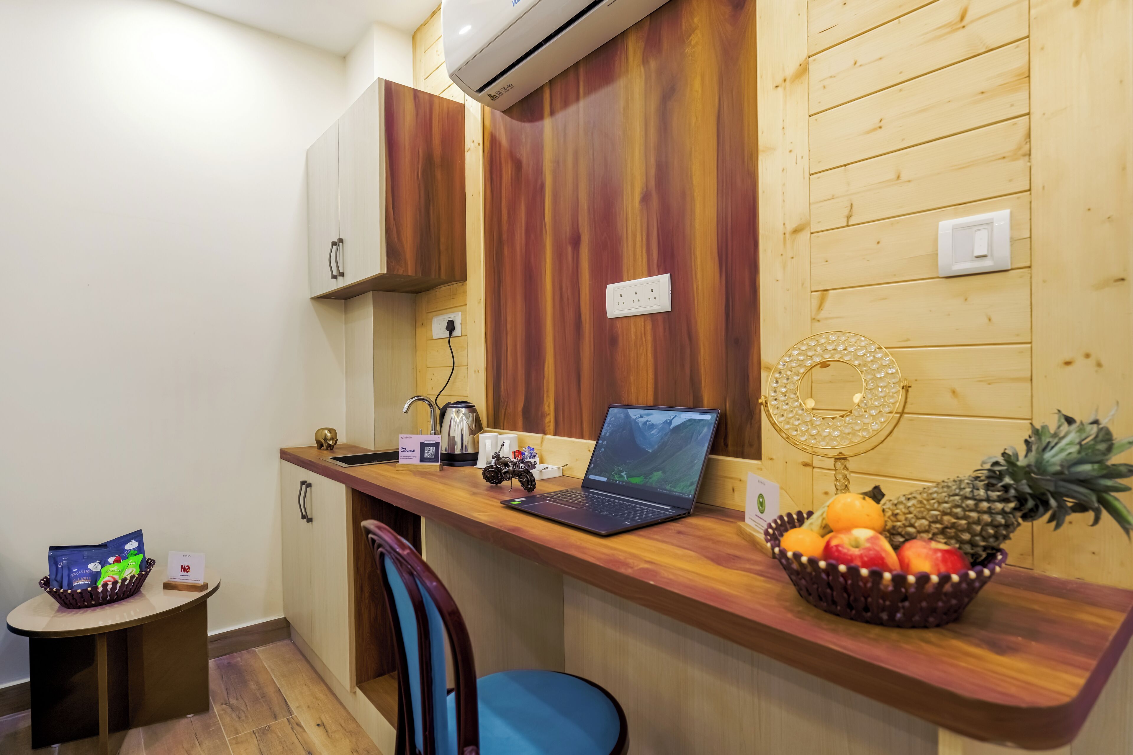 A compact kitchen with a laptop, a fruit bowl, and a small table with a bag of snacks.