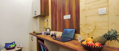 A compact kitchen with a laptop, a fruit bowl, and a small table with a bag of snacks.