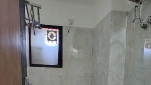 Een kleine badkamer met tegels, een toilet, een douche en een raam.