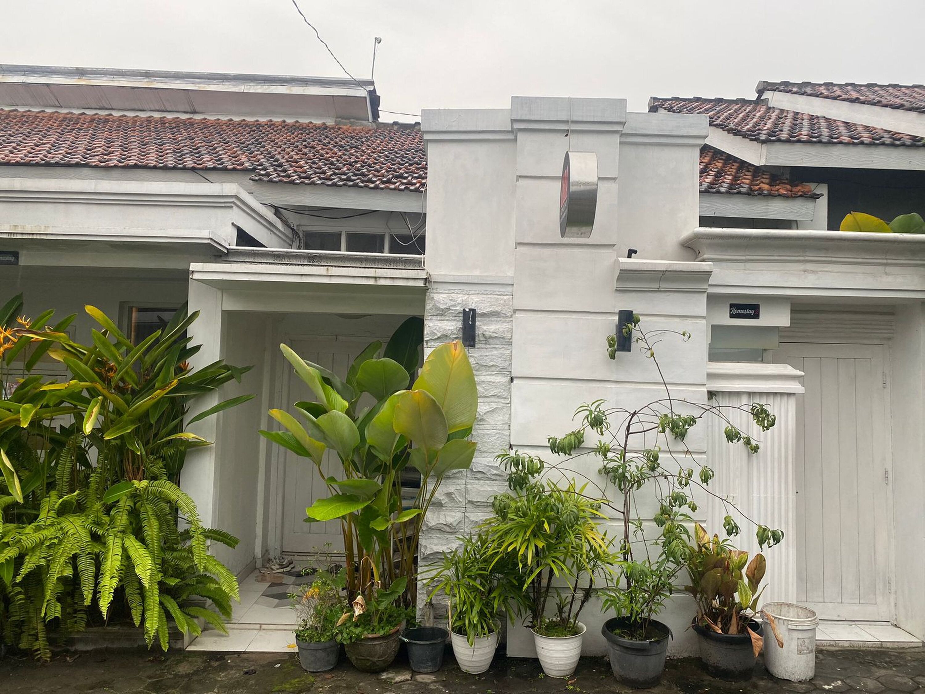 A white building with a tiled roof, surrounded by potted plants.