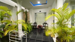 Un espace intérieur spacieux doté d’un sol carrelé, agrémenté de plantes en pot et comprenant un coin salon avec des chaises et une petite table.