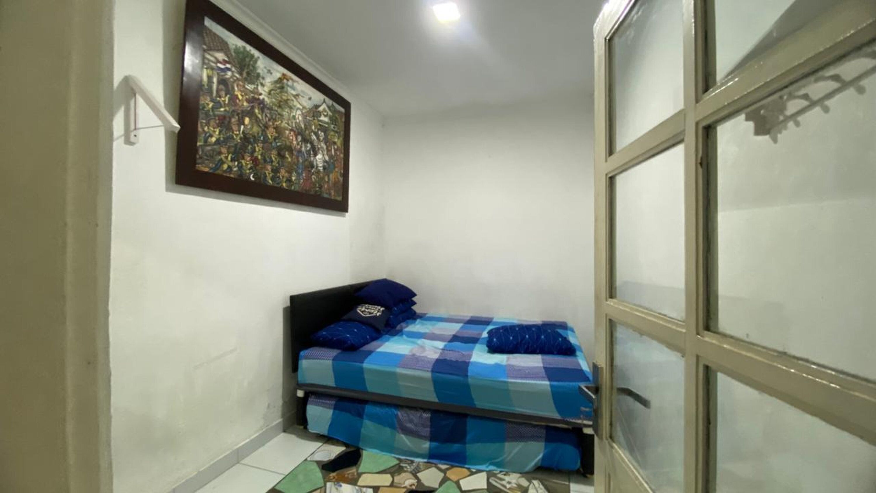 A small bedroom with a bed, a window, and a painting on the wall.