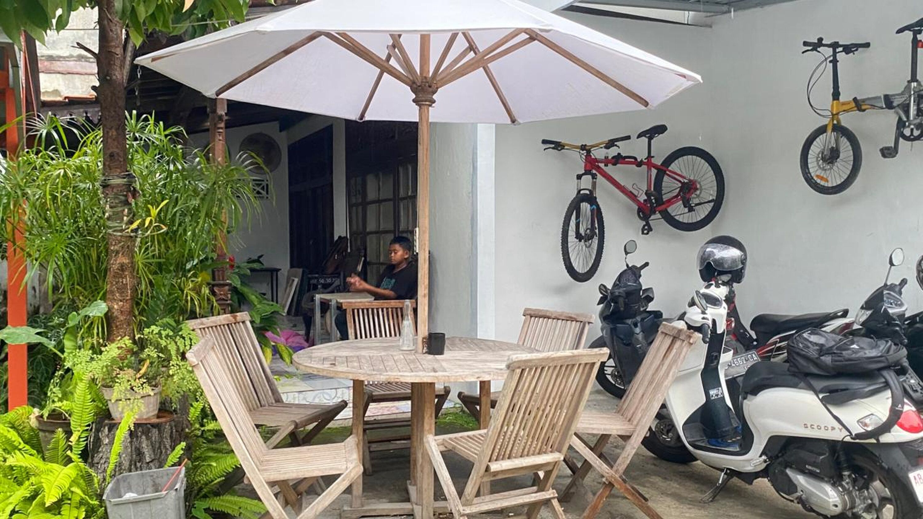 A patio with a round wooden table and chairs, an umbrella, and a wall-mounted bicycle.