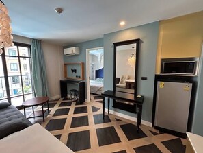 Ein Hotelzimmer mit schwarz-weiß kariertem Boden, einem Bett mit blau-weiß gestreifter Bettdecke, einem Schreibtisch mit Stuhl, einem kleinen Tisch, einem Spiegel, einem Fernseher und einem Kühlschrank.