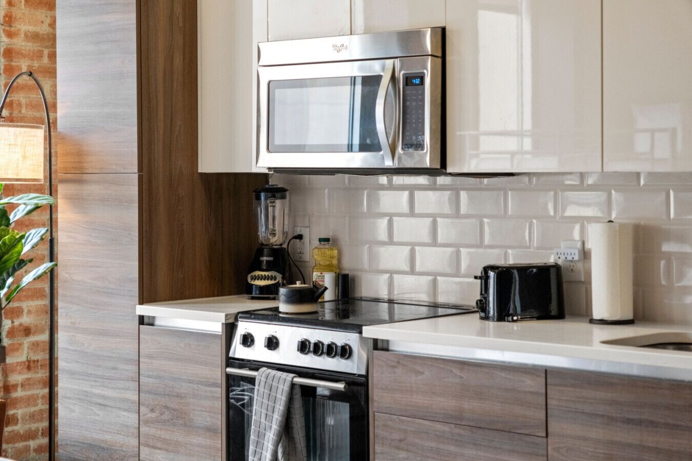 Cozinha moderna com eletrodomésticos de aço inoxidável, parede de tijolos e painel de azulejos branco.