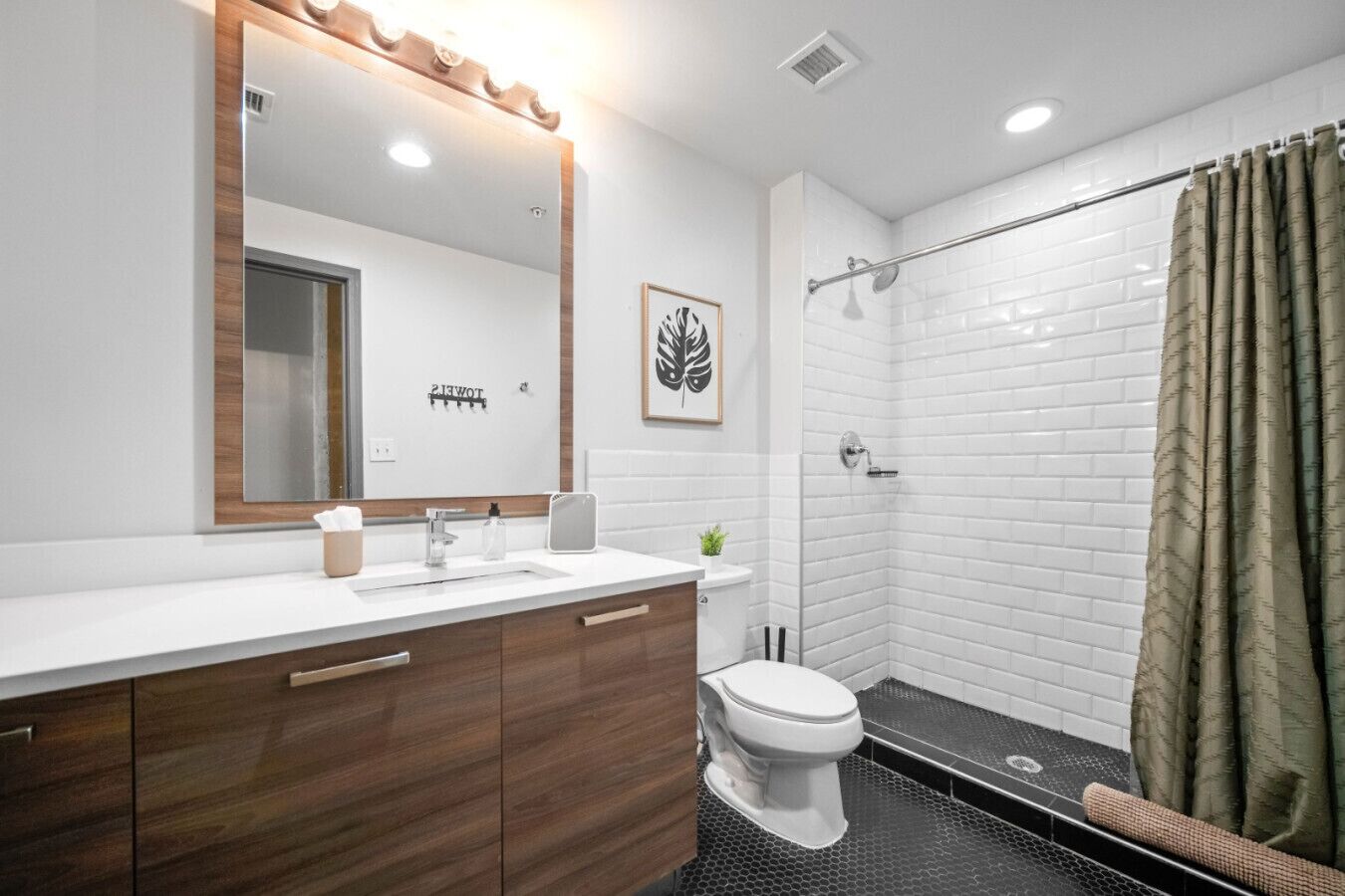 Een moderne badkamer met een wit wastafelmeubel, een toilet, een douche met glazen deur en een grote spiegel met verlichting.