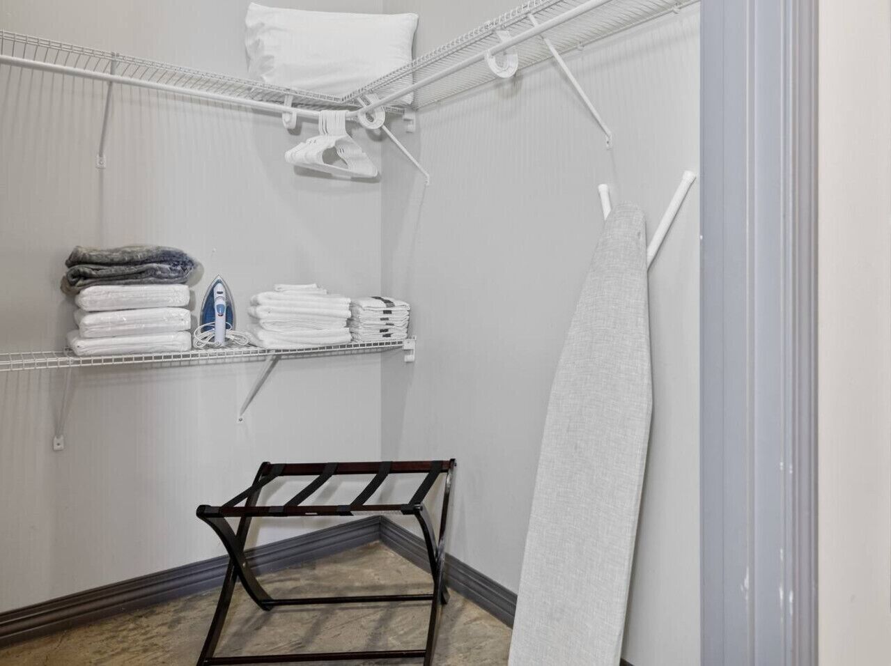 A laundry room with shelves holding folded towels and a hanging iron.