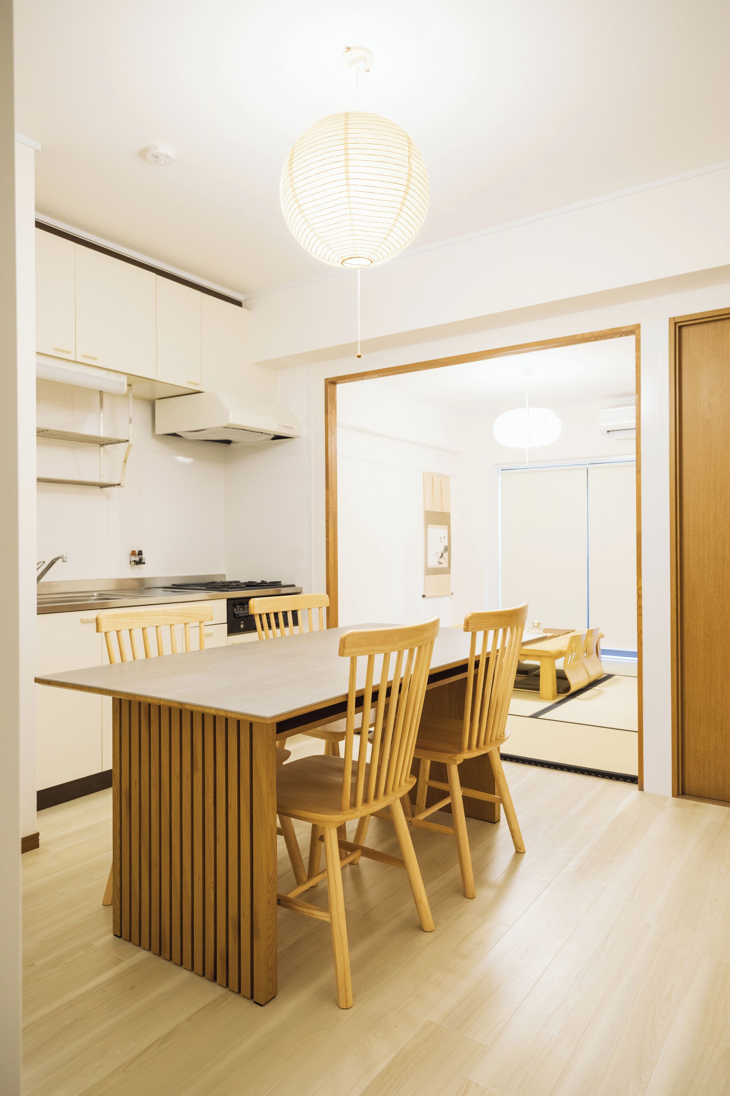 A modern kitchen with a wooden dining table and chairs, white cabinets, and a hanging light fixture.