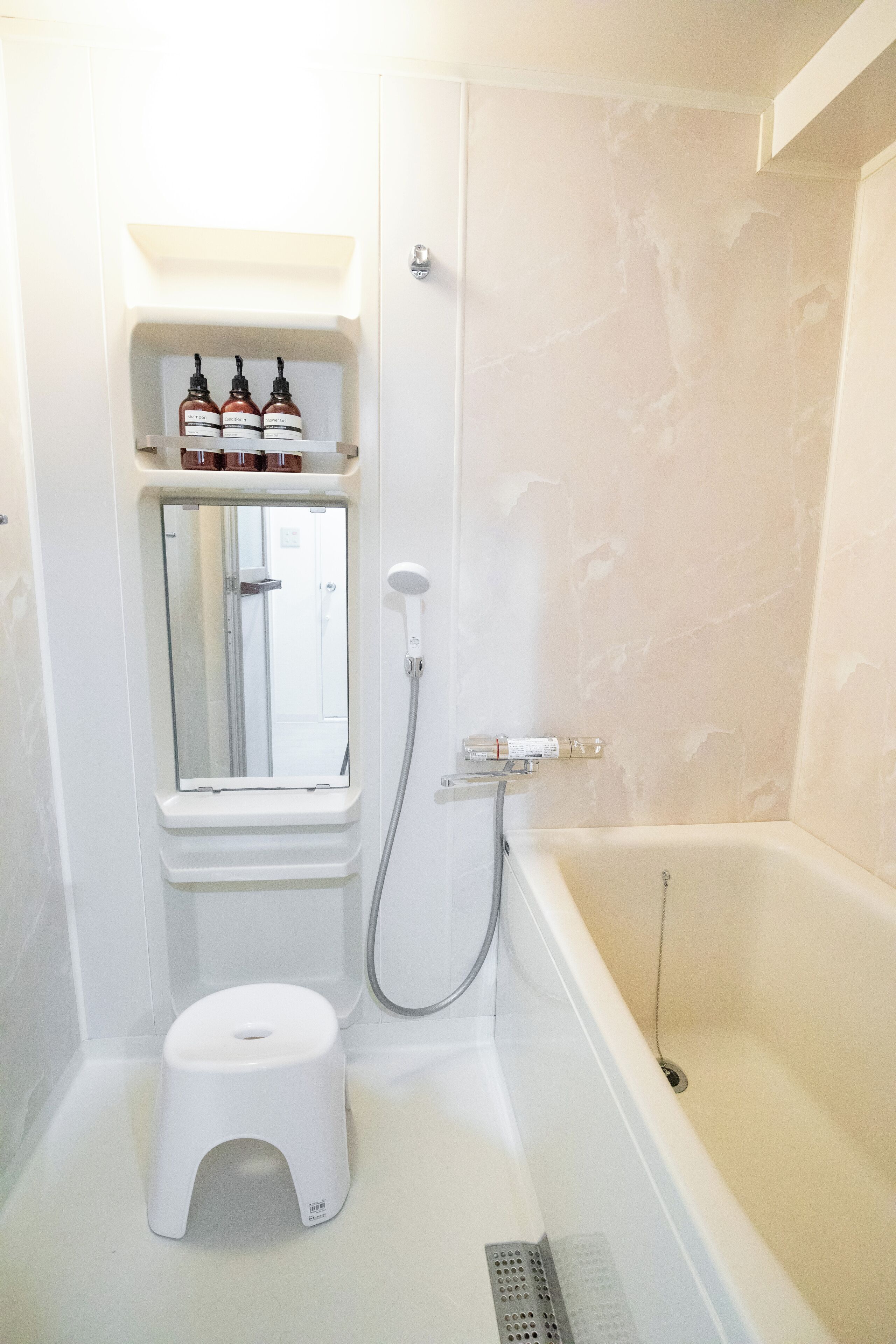A bathroom with a shower, toilet, and a shelf with bottles.