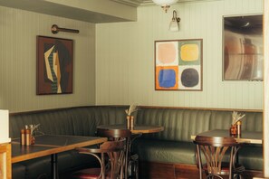 A corner seating area with a green upholstered bench, wooden tables, and chairs. - The Kithmore Hotel (St. Andrews)