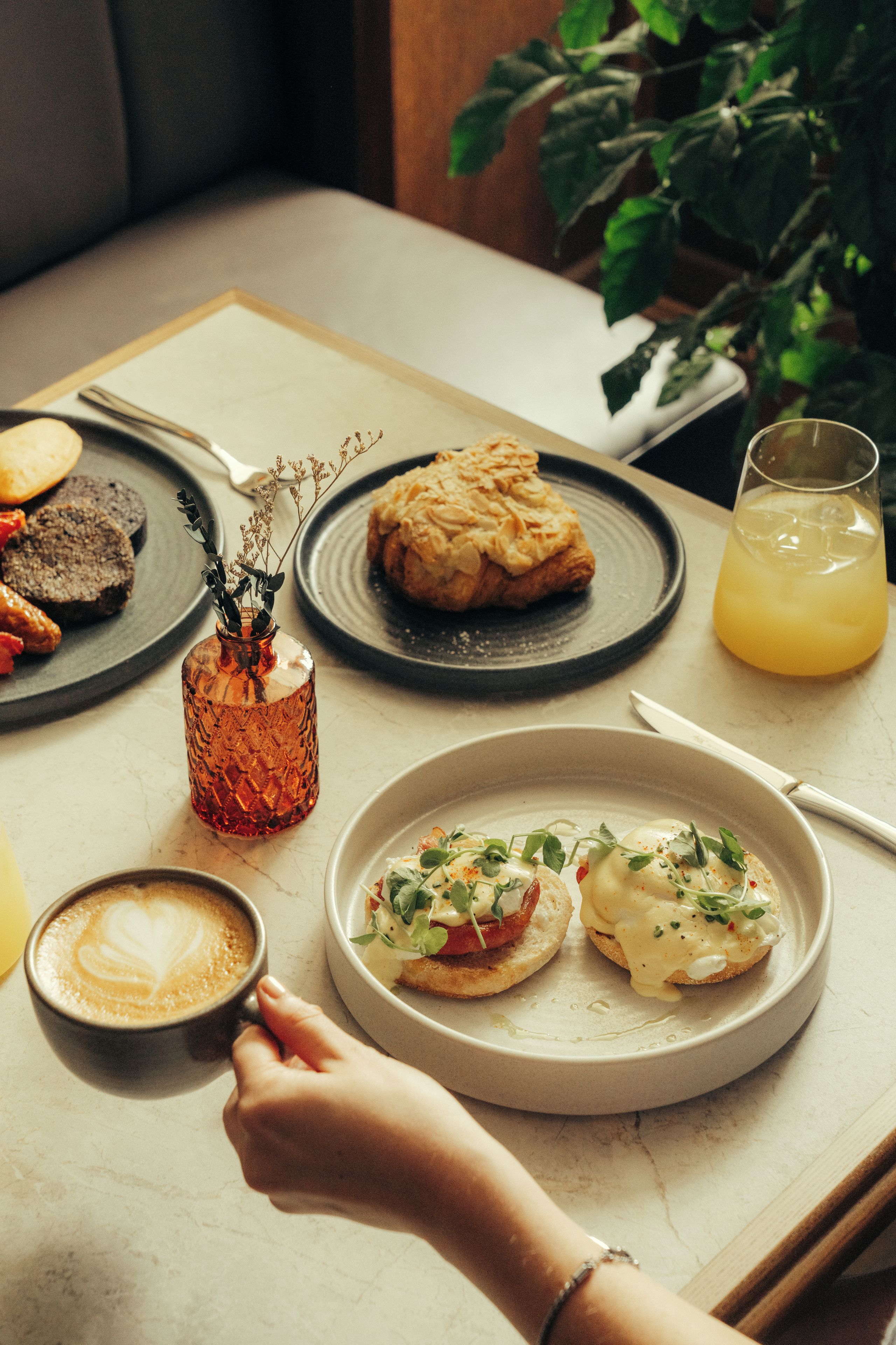 Uma mesa posta para o café da manhã, com ovos Benedict, um croissant e um copo de suco de laranja.