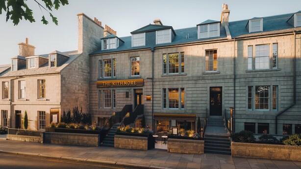 Ein mehrstöckiges Hotel mit einer steinernen Fassade, einem Schild mit der Aufschrift 'The Kitmore' und einer Treppe, die zum Eingang führt.
