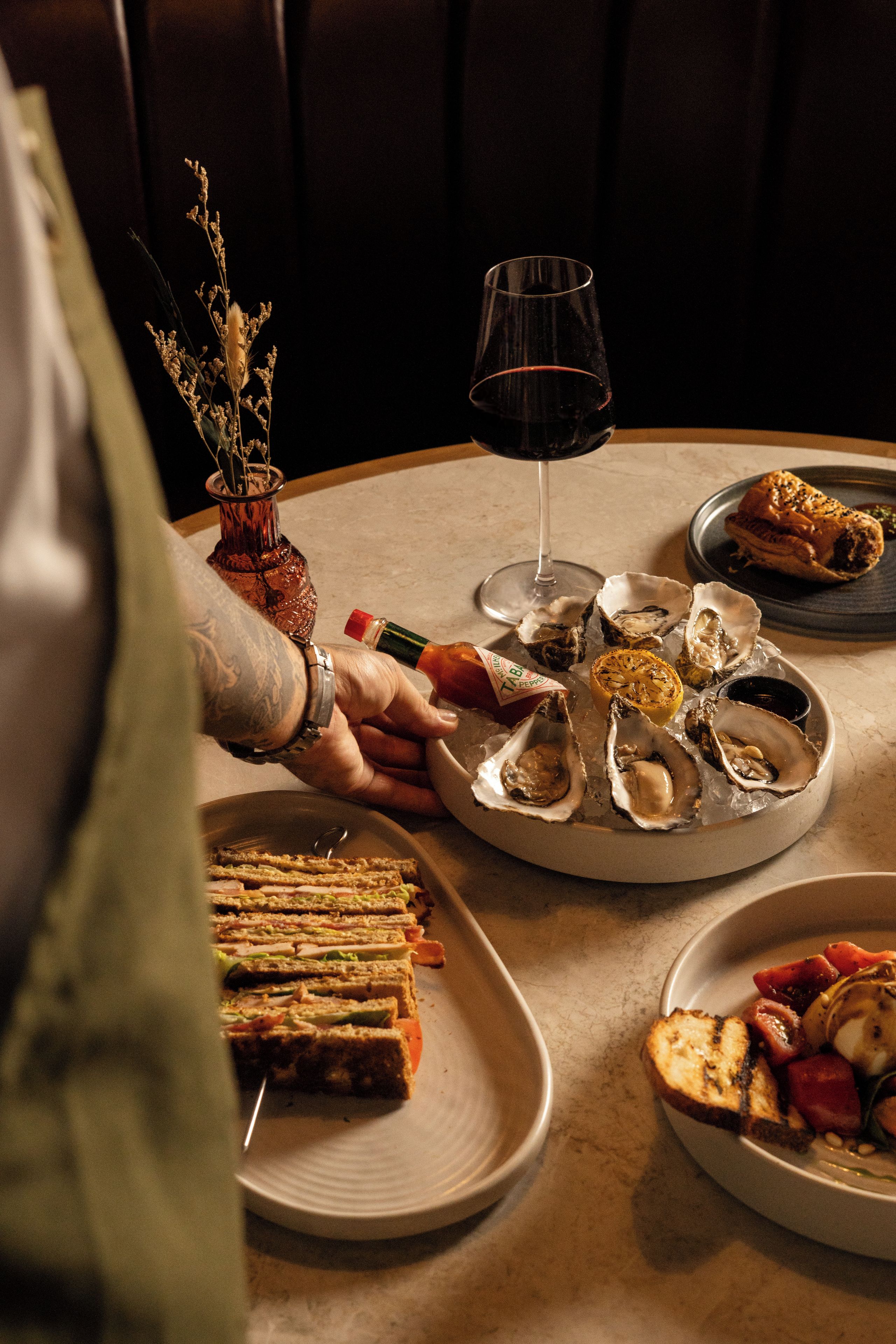 Una mesa de comedor con platos de comida, una copa de vino tinto y una botella de agua.