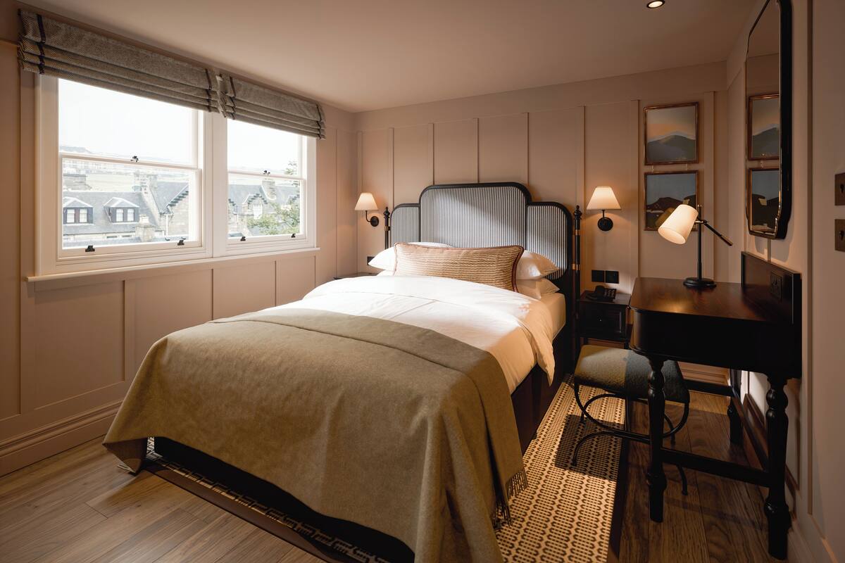 A bedroom with a bed, bedside lamps, a desk, and a chair.