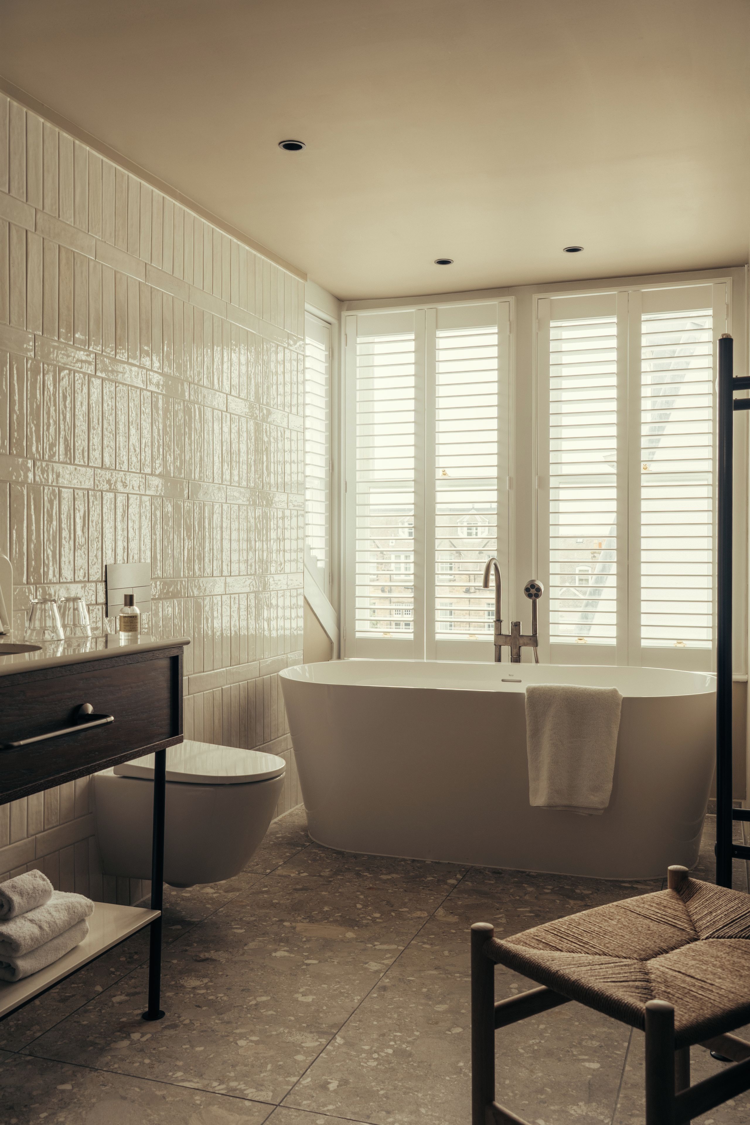 A bathroom with a freestanding bathtub, a vanity with a mirror, and a window with blinds.