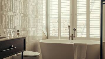 A bathroom with a freestanding bathtub, a vanity with a mirror, and a window with blinds.