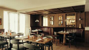 Un restaurante con paneles de madera, asientos tipo cabina de cuero y una zona de bar con luces colgantes.