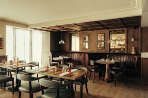 Un restaurante con paneles de madera, asientos tipo cabina de cuero y una zona de bar con luces colgantes.
